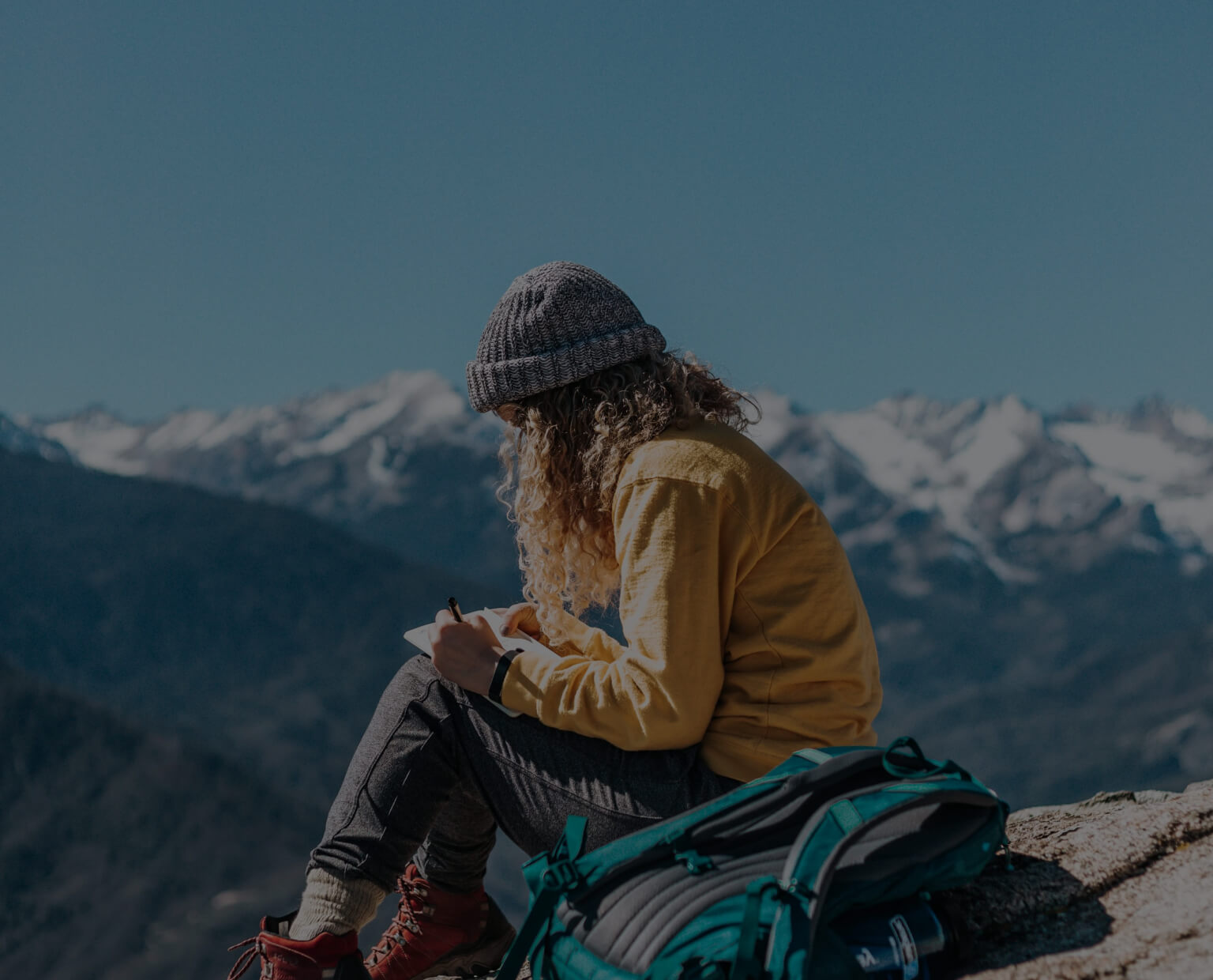 Mulher escreve em caderno no topo da montanha.